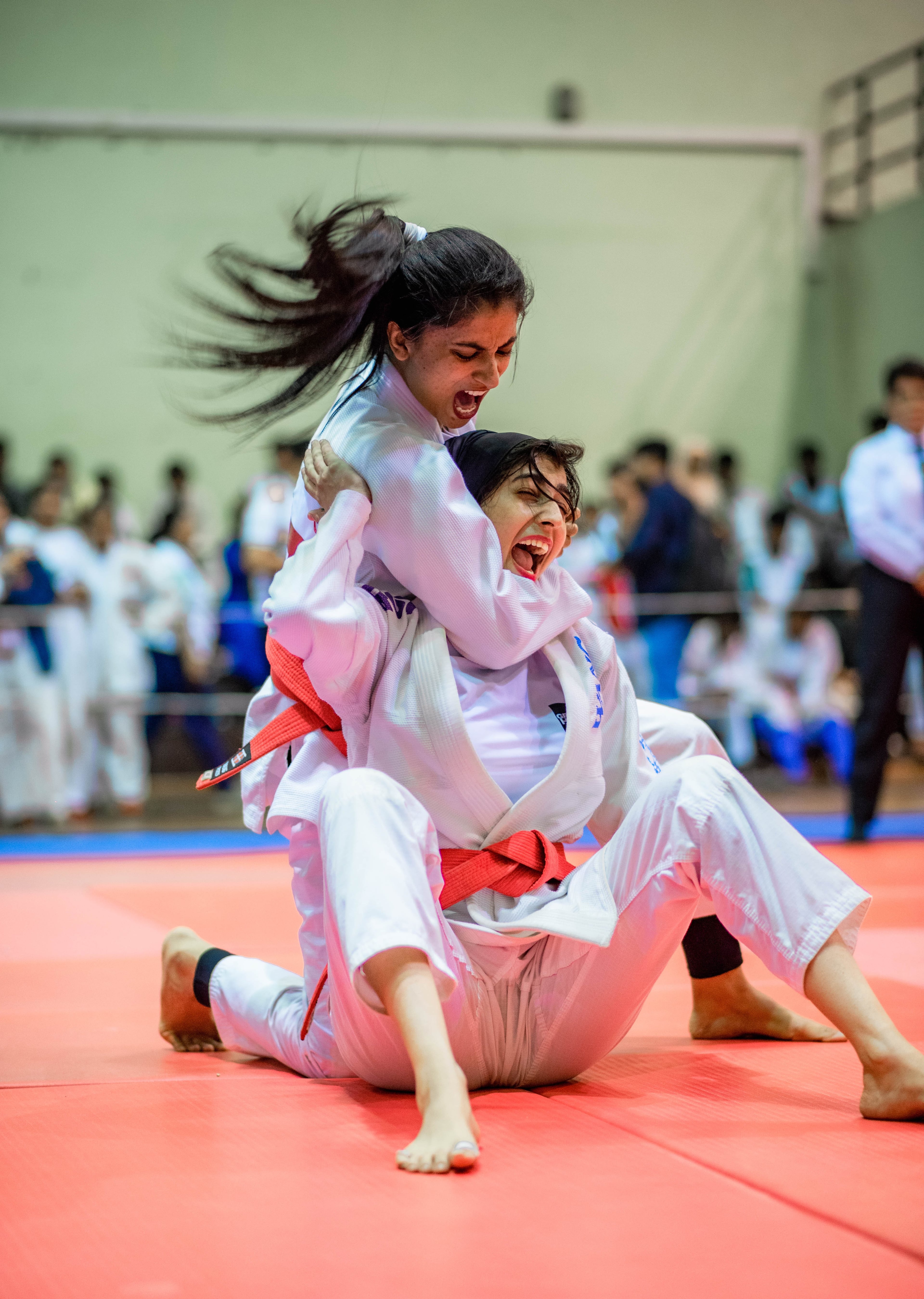 A jujitsu athlete driven to the mat mid-throw, hair flying, the hall packed behind